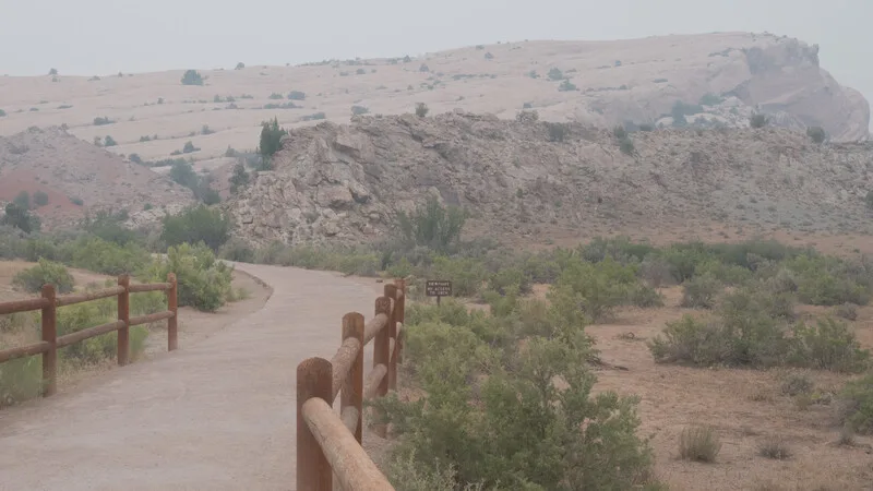 Rustic wooden fence railing along a dusty path with arid hillside landscape