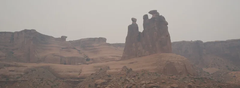 Towering red rock formations rise from desert landscape under hazy sky