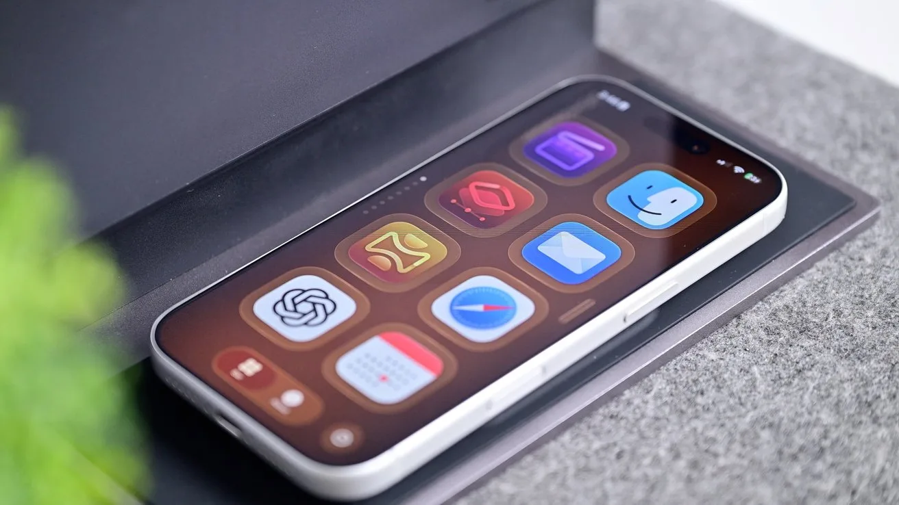 Smartphone lying on a table, screen facing up, displaying colorful rounded app icons on a dark background, with a blurred green plant in the corner and soft indoor lighting