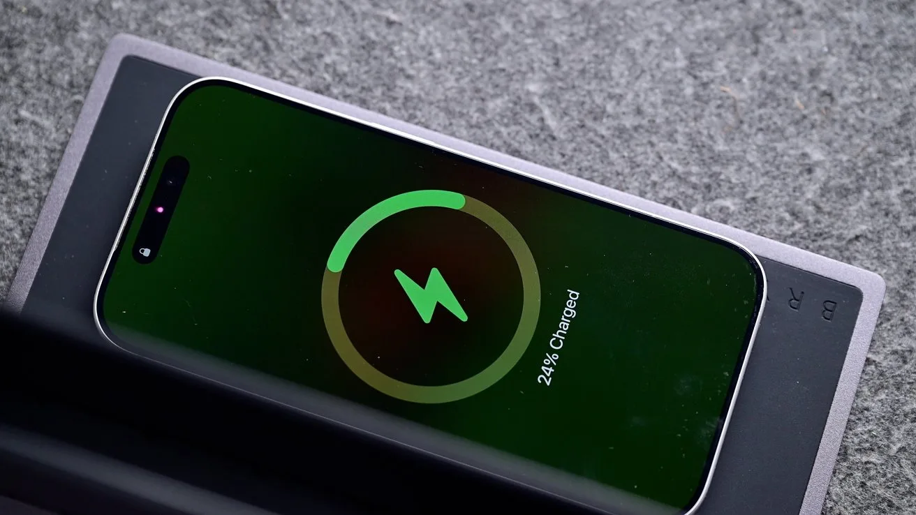 Smartphone lying on a wireless charging pad, screen showing a large green circular charging icon and text indicating 24 percent charged, set on a gray textured surface