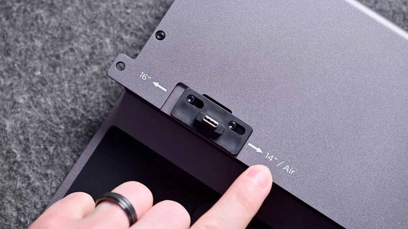 Finger pointing at a small USB-C style connector on a gray metal device, with engraved labels and arrows indicating 16 and 14 / Air size positions on the surface