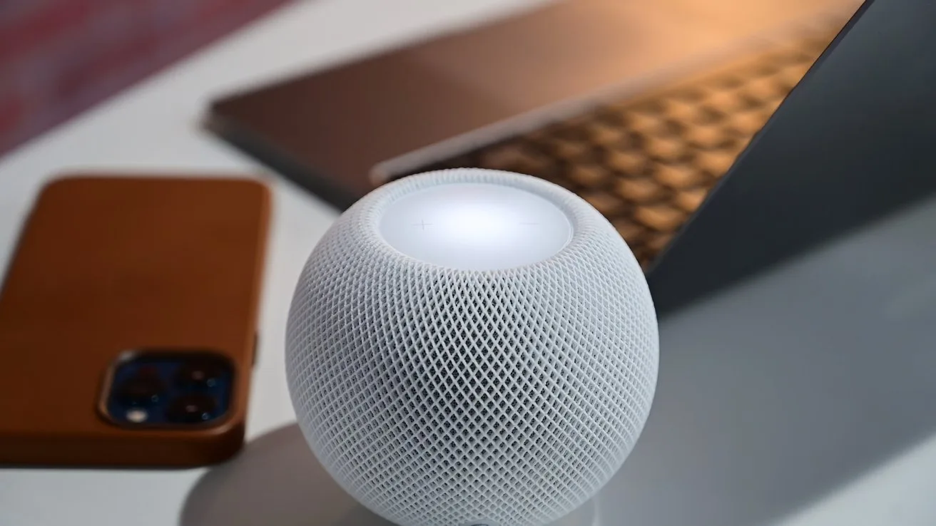 White spherical smart speaker glowing on top, placed on a desk beside a brown-cased smartphone and an open laptop with metallic keyboard