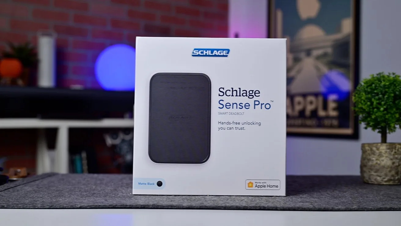 Box of Schlage Sense Pro smart lock on a table in a modern living room, with blurred shelves, decorations, and framed wall art in the background