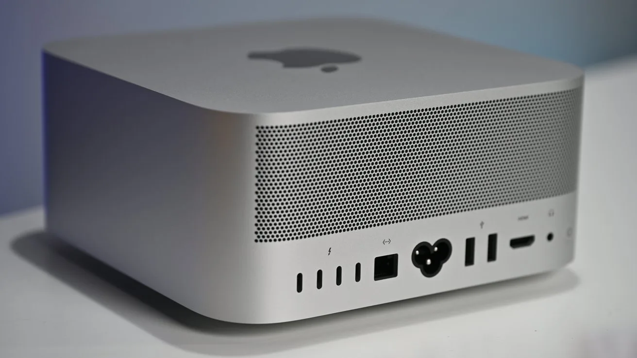 Silver Apple desktop computer with perforated back panel, multiple ports including USB, Thunderbolt, HDMI, Ethernet, and power connector, resting on a white surface against a soft blue background