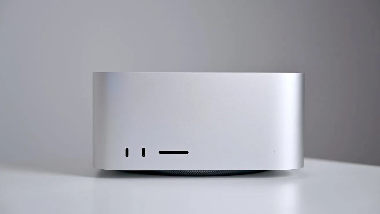 Silver rectangular desktop computer with rounded corners on a white surface against a light gray background, showing front ports and power indicator on the lower left and right sides