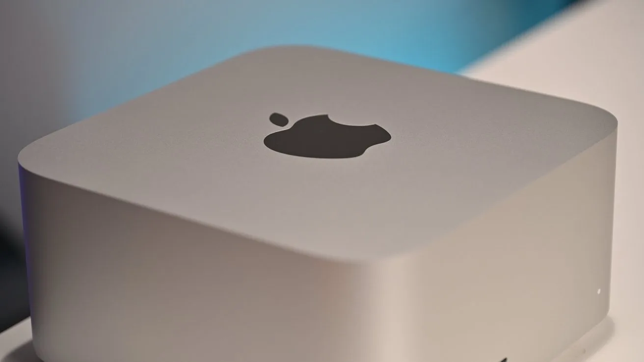 Silver Apple Mac mini desktop computer with rounded edges, viewed close up from above, showing the black Apple logo centered on the top surface against a softly lit background