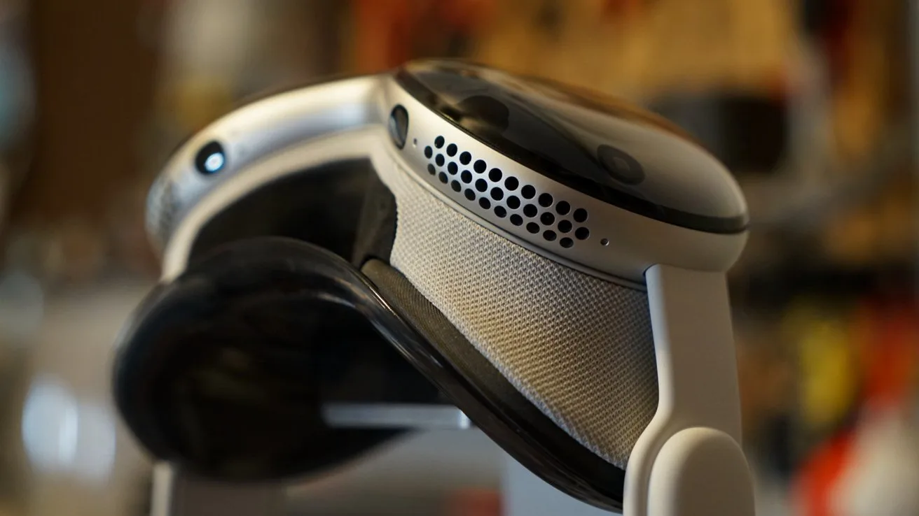 Close-up of Apple Vision Pro, showing curved glass front, perforated speaker vents, and padded fabric band in warm indoor lighting, emphasizing modern, high-tech design