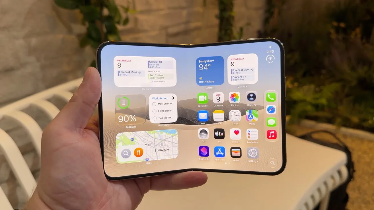 Hand holding a large foldable smartphone fully open, showing a bright home screen with multiple app icons and widgets, against an outdoor patio background with white furniture and green plants