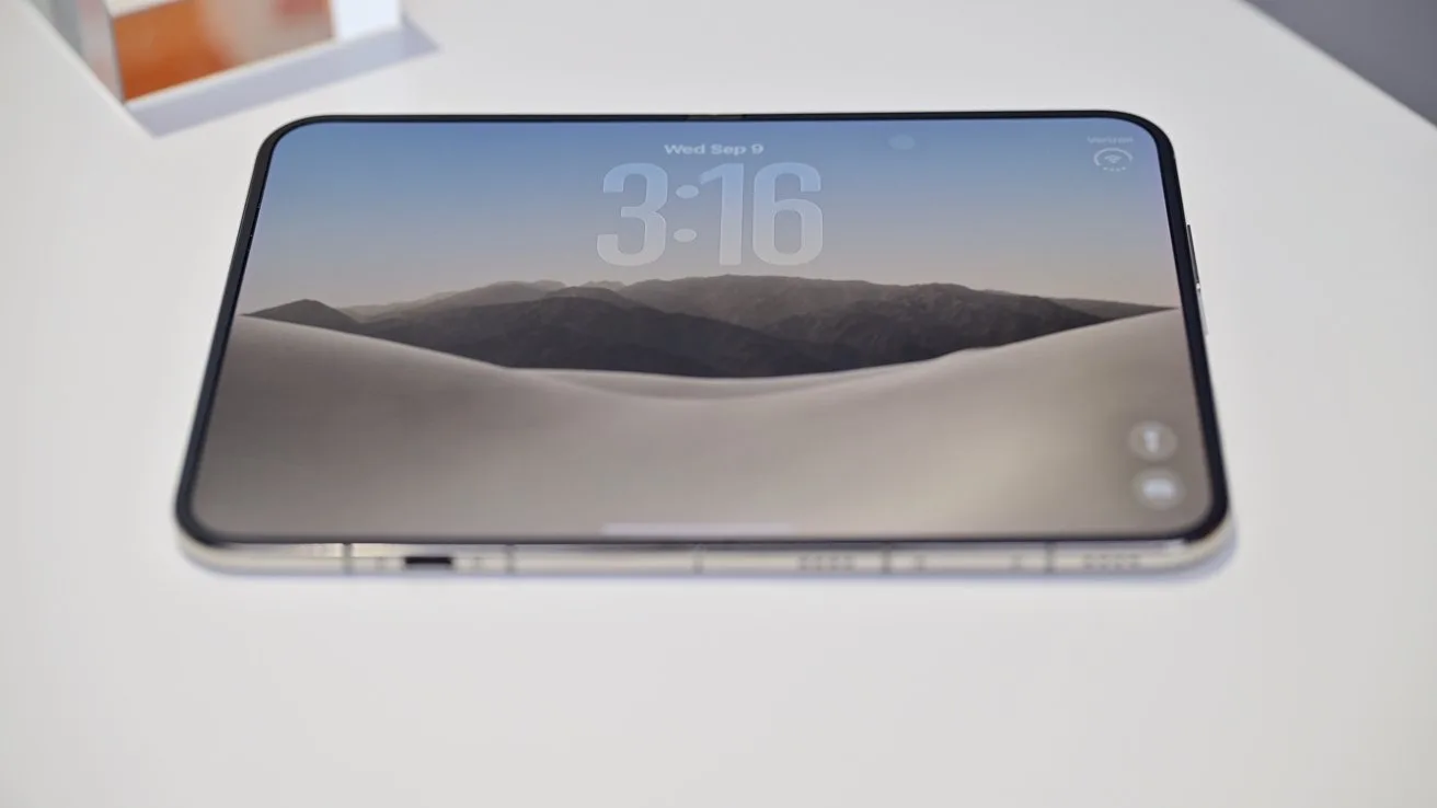 Smartphone lying flat on a white surface, screen on, displaying a minimalist desert landscape wallpaper with distant mountains and large digital clock reading 3:16 at the top