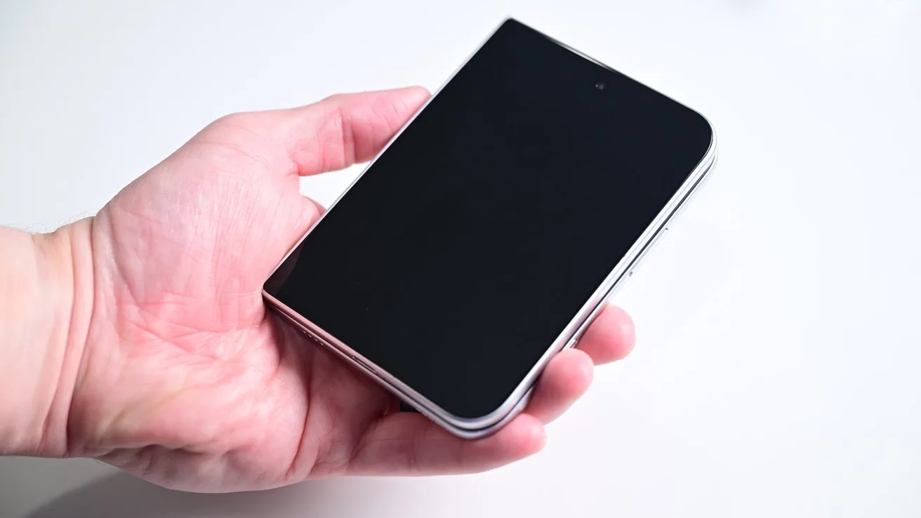 A person's hand holding a closed, black foldable smartphone with rounded corners against a plain white background