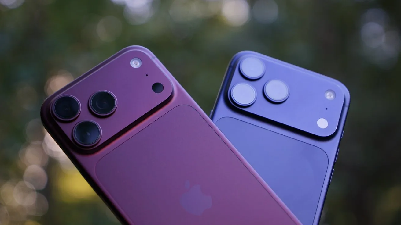 A burgundy iPhone 18 Pro Max and blue iPhone 17 Pro Max shown from the back with large dual camera modules, held side by side against a softly blurred green outdoor background