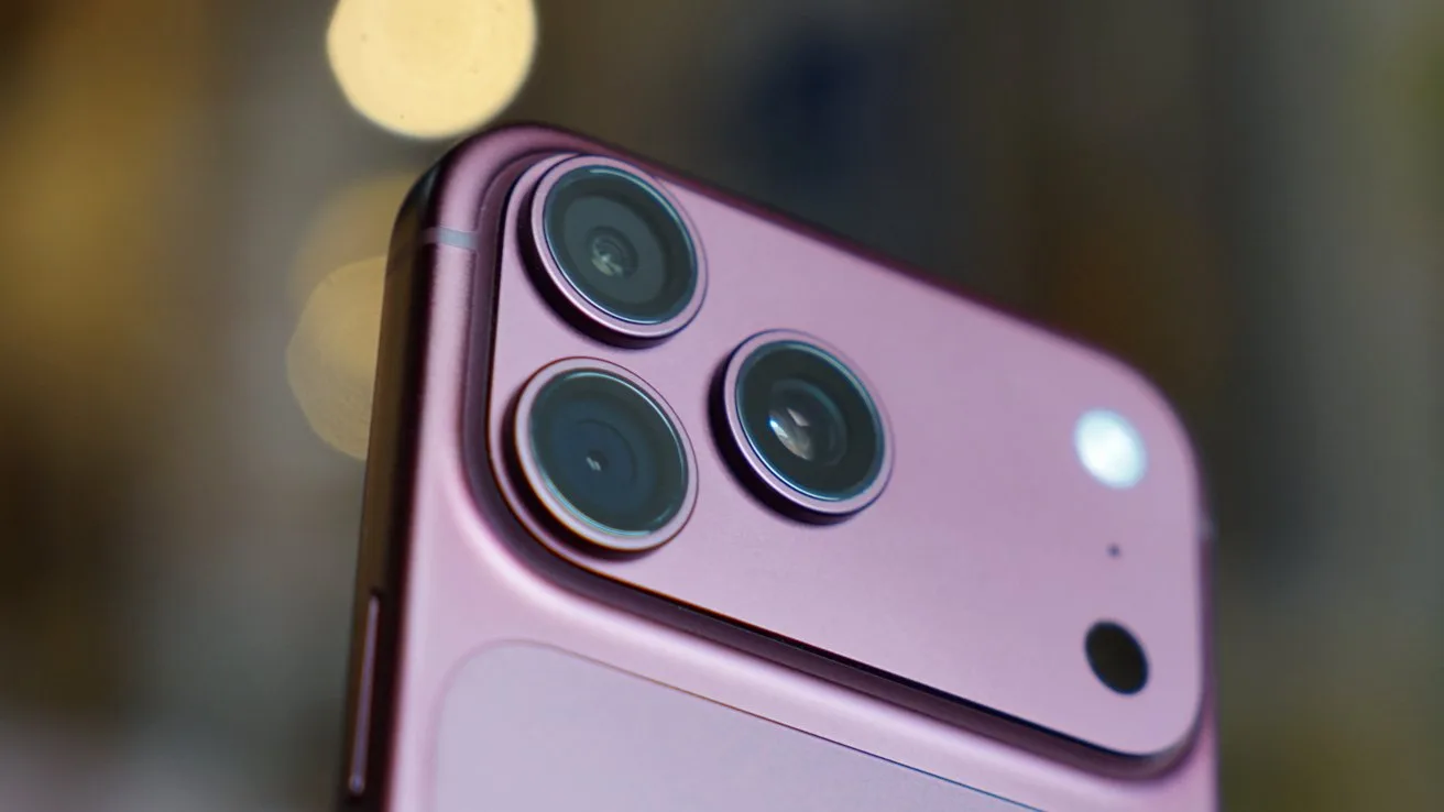Close-up of a burgundy iPhone 18 Pro Max rear camera module, showing three prominent lenses and a small sensor against a softly blurred background with warm circular light bokeh