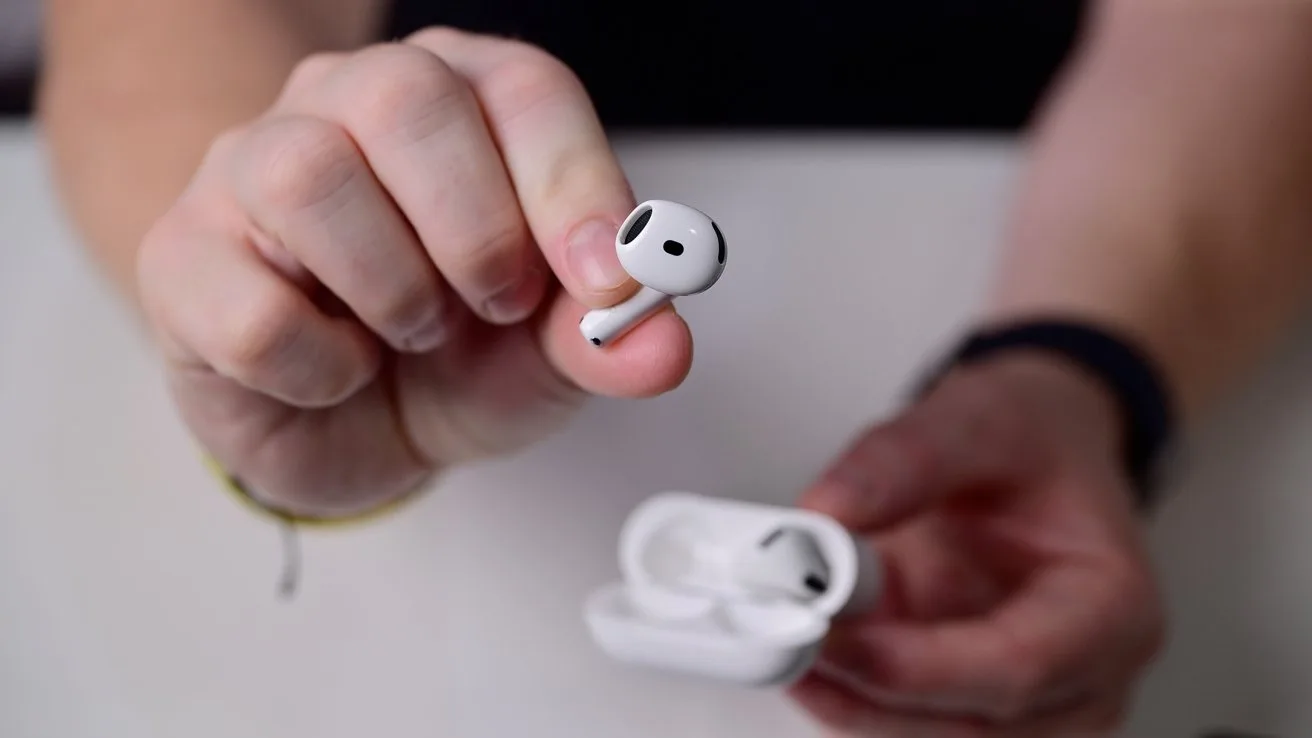 Hand holding a single white wireless earbud close to the camera, with the other earbud and open charging case resting in the same hand against a plain background