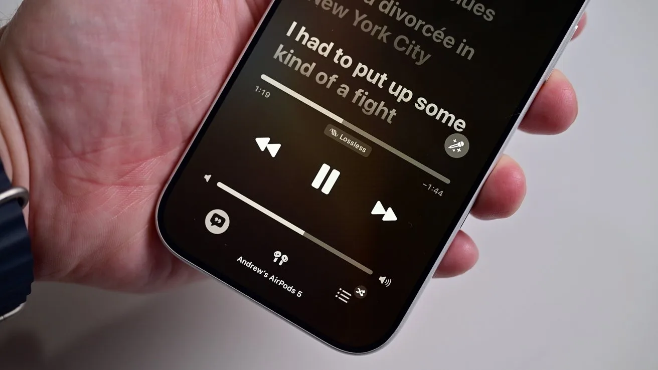 Hand holding a smartphone displaying a dark music player screen with large white song lyrics, play and skip controls, and volume slider visible near the bottom