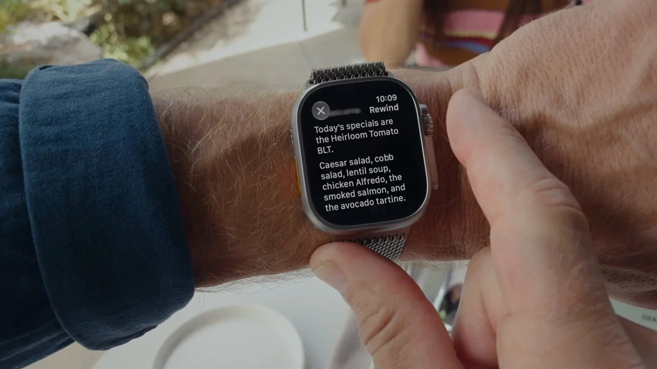 A person wearing an Apple Watch reads a restaurant notification listing daily specials, with another hand touching the screen while seated at an outdoor table with plates in the background