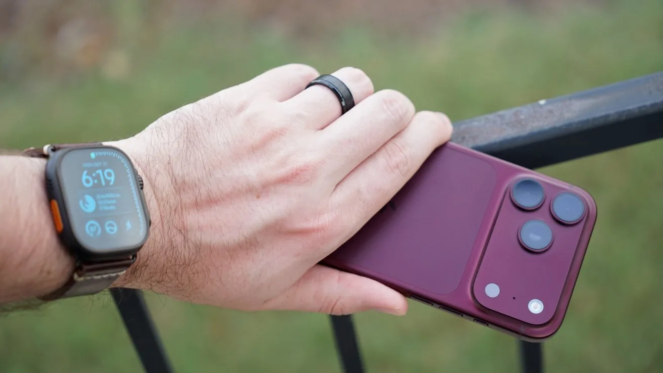 Hand resting on a railing, wearing an Apple Watch Ultra 4 and dark ring, holding a burgundy iPhone 18 Pro with three rear cameras against a blurred outdoor background