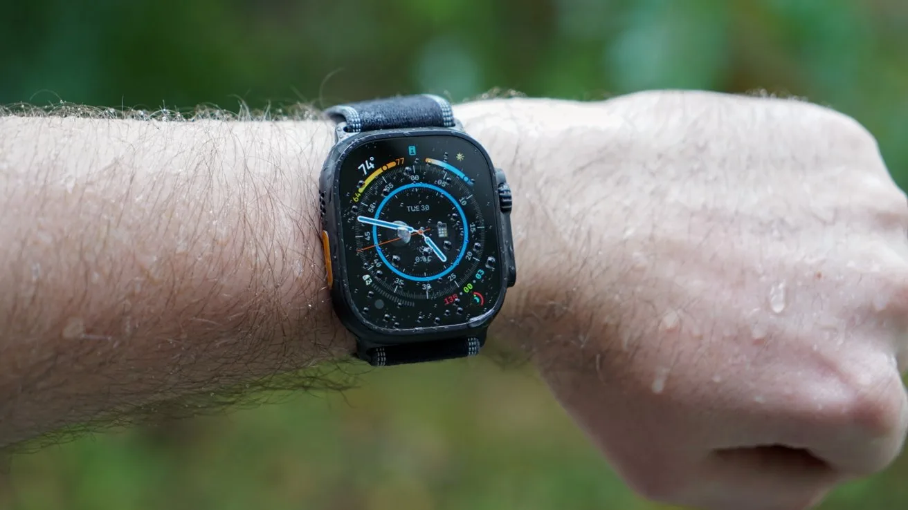 Close-up of a person's wrist wearing an Apple Watch Ultra 3 with a colorful circular digital dial, seen outdoors with raindrops on the skin and a blurred green background
