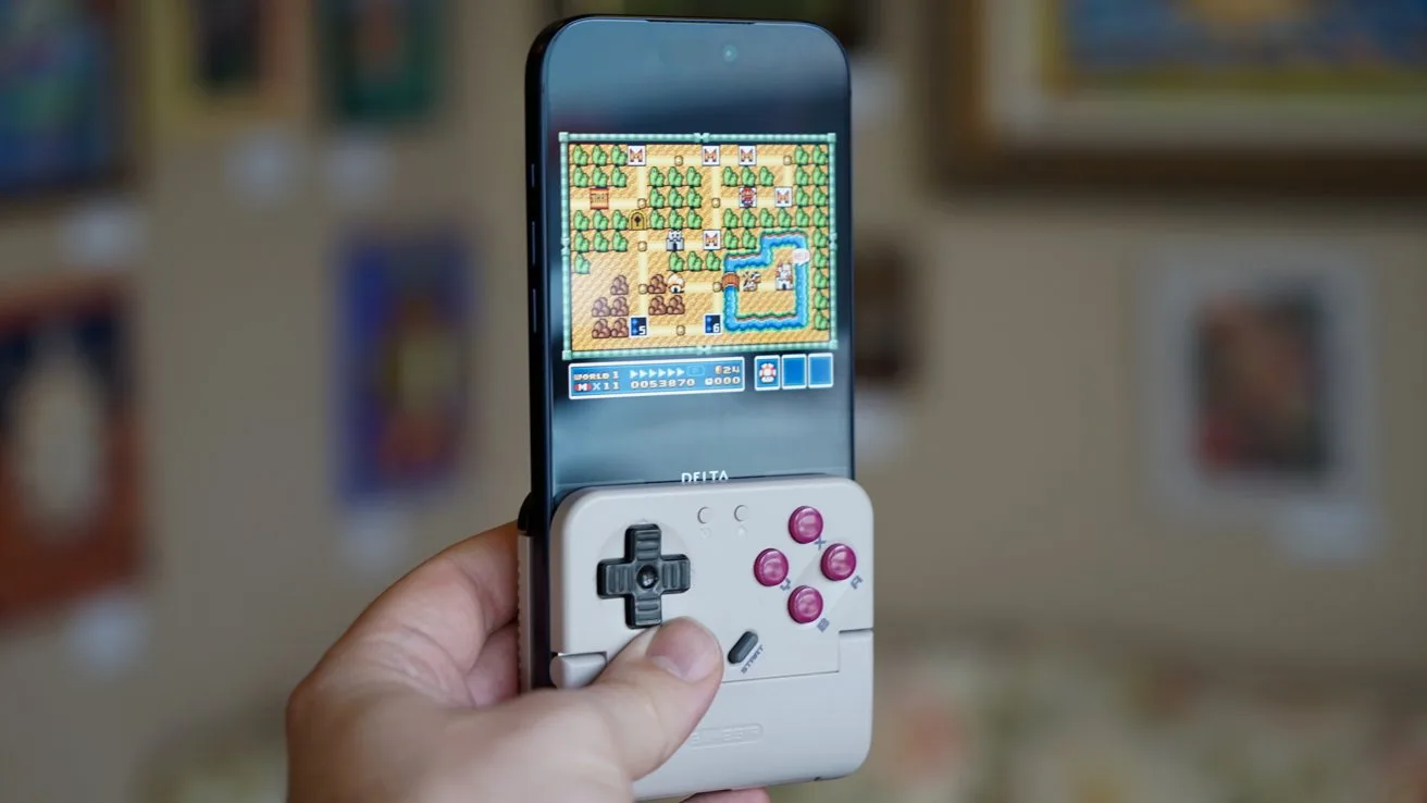 Hand holding an iPhone 17 Pro Max with a retro-style game controller attached, displaying a colorful pixelated adventure game screen, in a softly focused living room with framed artwork on the walls