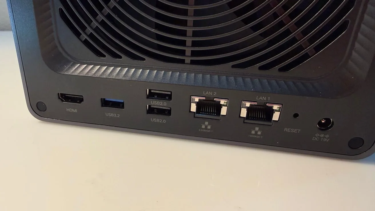Back panel of a network device showing a large cooling fan, HDMI port, USB ports, two Ethernet LAN ports, a reset button, and a round power connector on a white surface