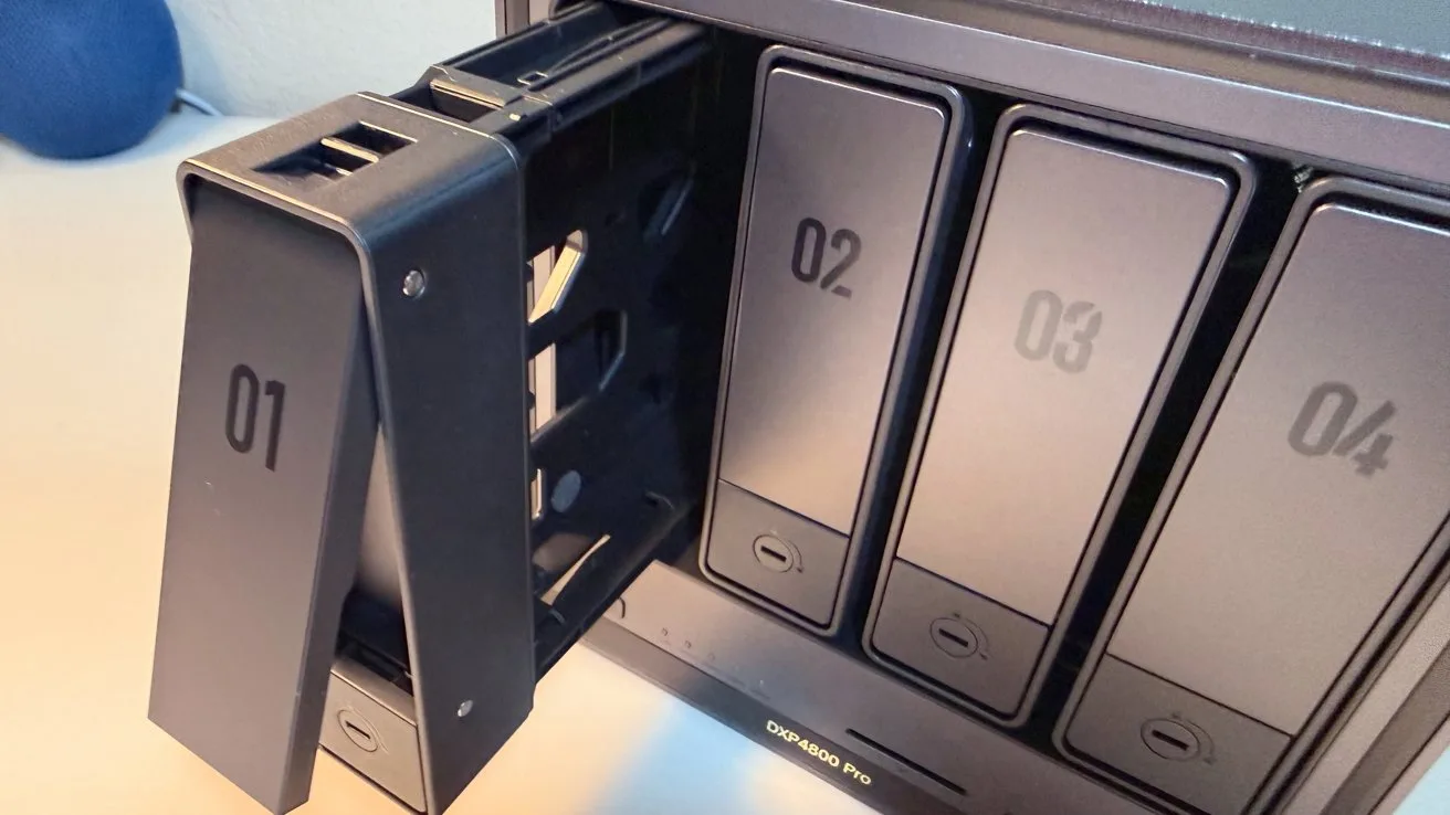 Close-up of a multi-bay network storage device, with drive bay 01 pulled out on a metal tray, and bays 02, 03, and 04 still closed in the enclosure