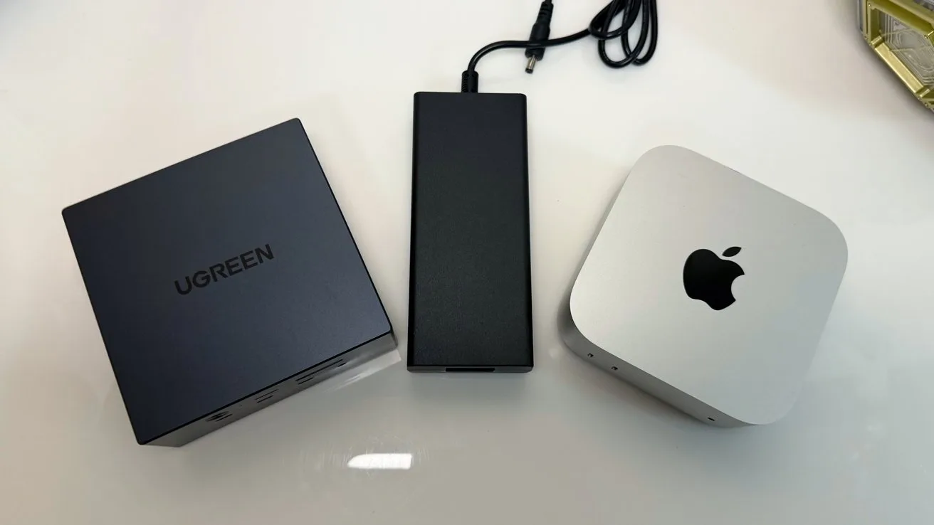 Three small desktop devices on a white surface: a dark gray UGREEN box, a slim black power adapter with cable, and a silver Apple Mac mini with black Apple logo