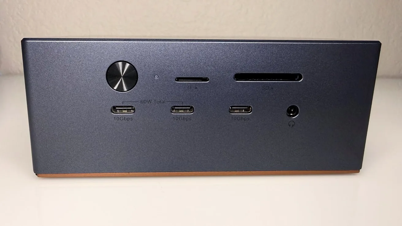 Small dark gray desktop hub with round power button, multiple USB-C ports, SD and microSD card slots, audio jack, and power connector on a clean white surface