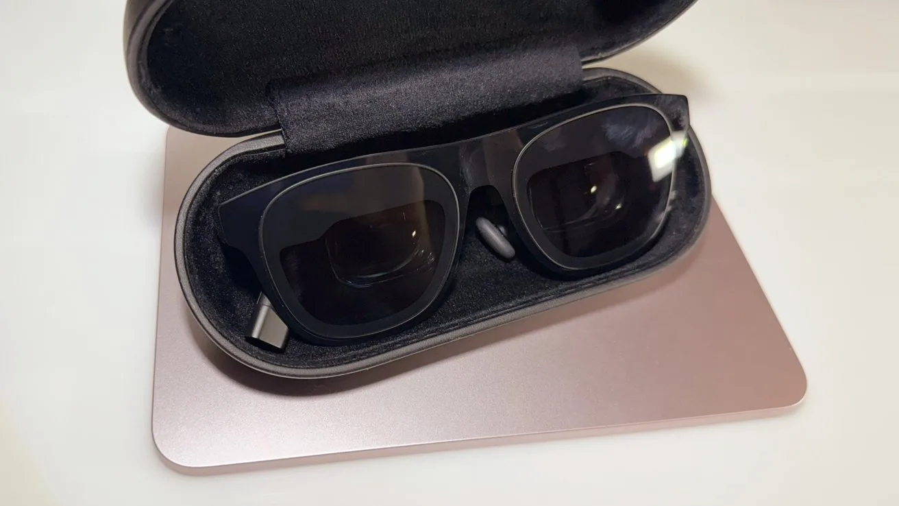 Black sunglasses in an open black case resting on a closed silver laptop on a white surface.