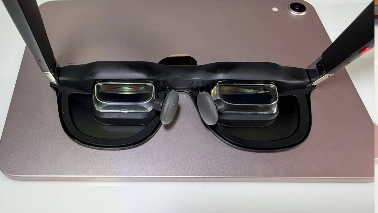AR glasses with transparent lenses and black frame placed on a metallic surface, viewed from above.