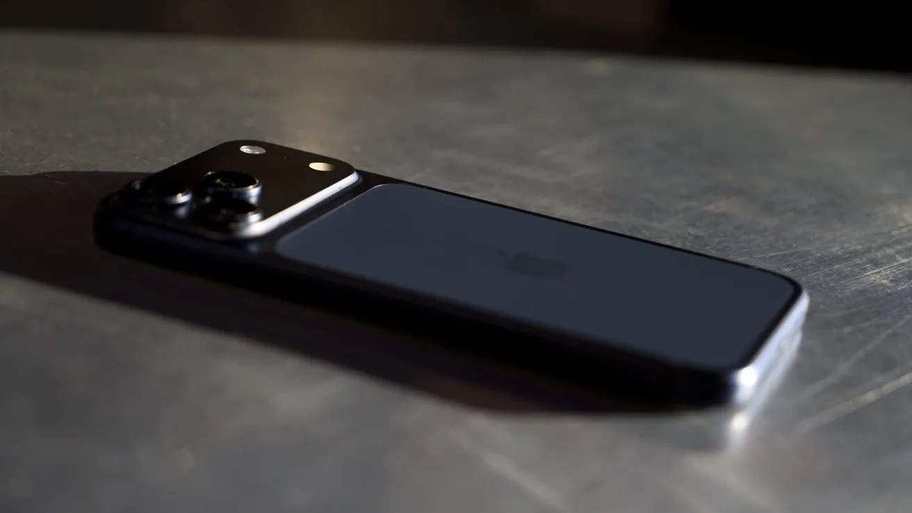 iPhone 17 Pro Max lying face down on a reflective metal surface, with a raised rear camera module catching light and casting a soft shadow in a dimly lit setting