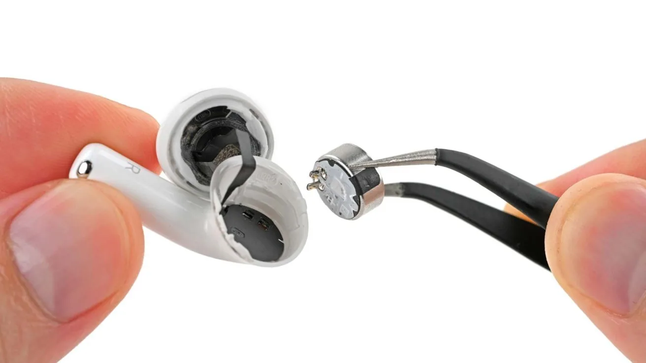 Hand holding a sliced open AirPod earbud while tweezers hold a removed circular battery