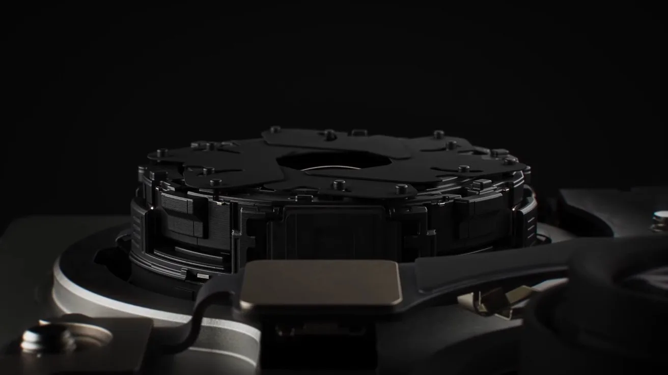 Close-up of a dark mechanical component with intricate circular parts and cables, set against a black background, resembling the internal mechanism of high-tech electronic or optical equipment