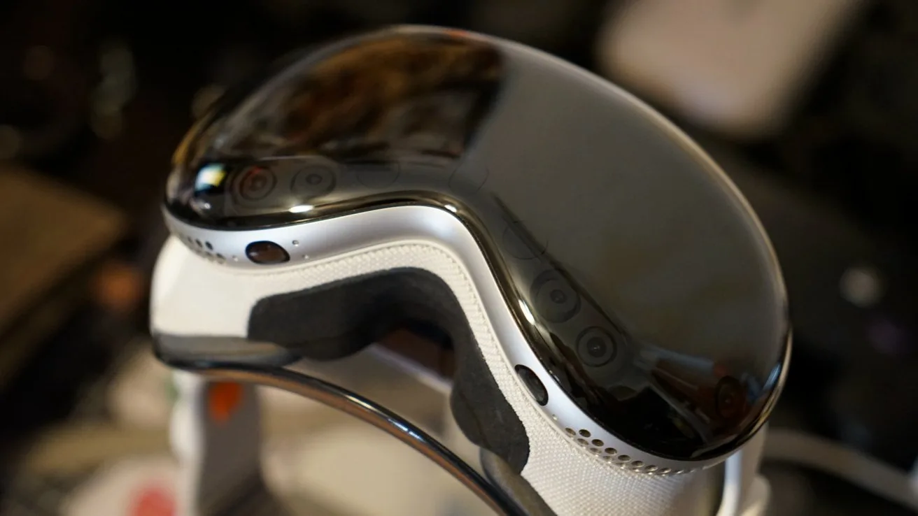 Close-up of an Apple Vision Pro with a shiny curved visor, white padding, and ventilation holes, resting on a dark, blurred background