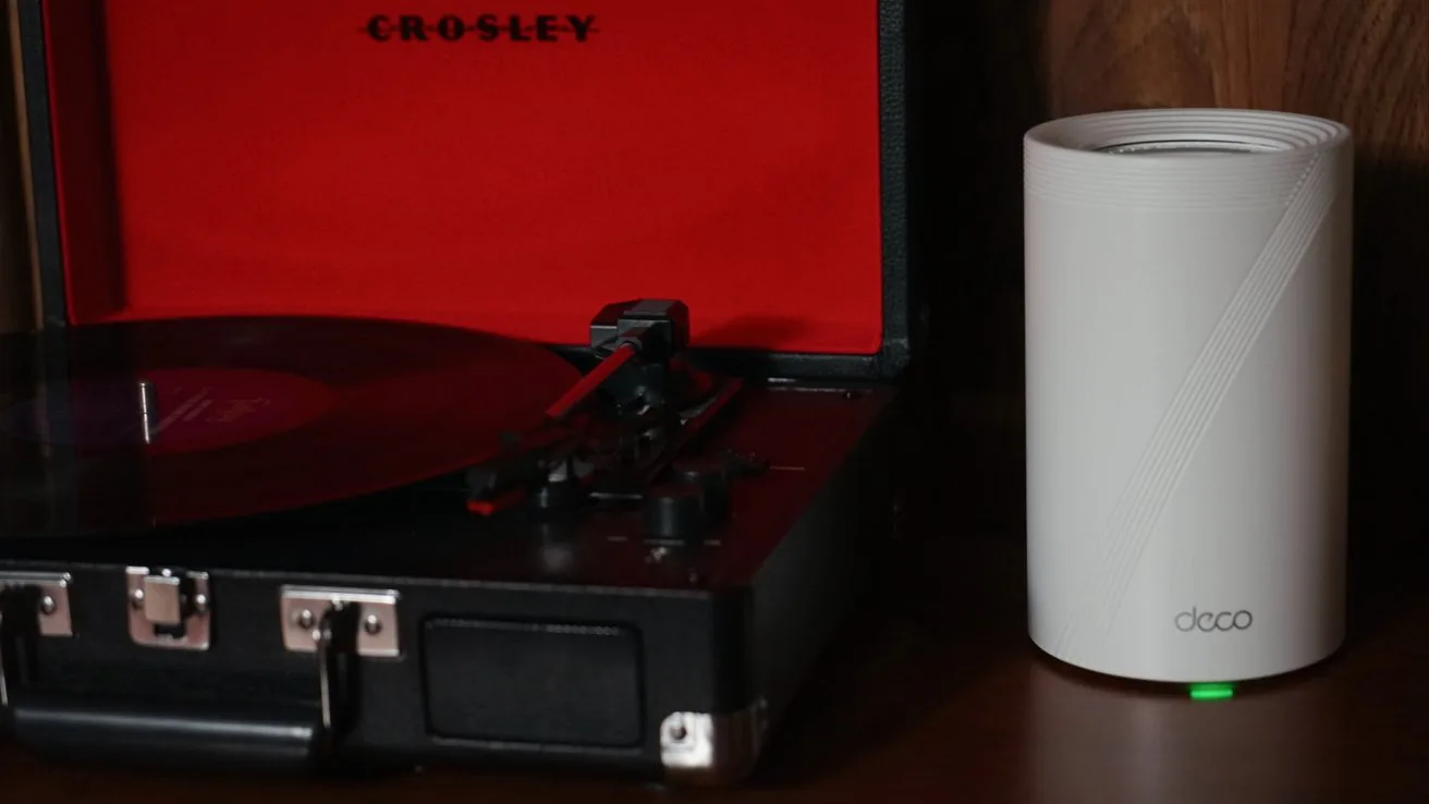 Record player with lid open, playing a vinyl record next to a cylindrical white electronic device on a wooden surface.