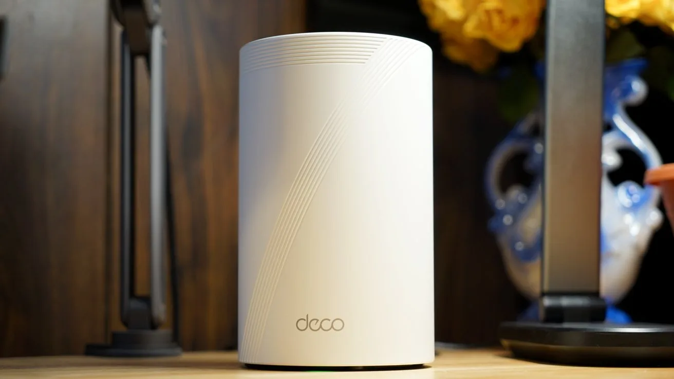 White cylindrical device with subtle diagonal lines on a wooden surface, surrounded by decorative items and soft lighting.