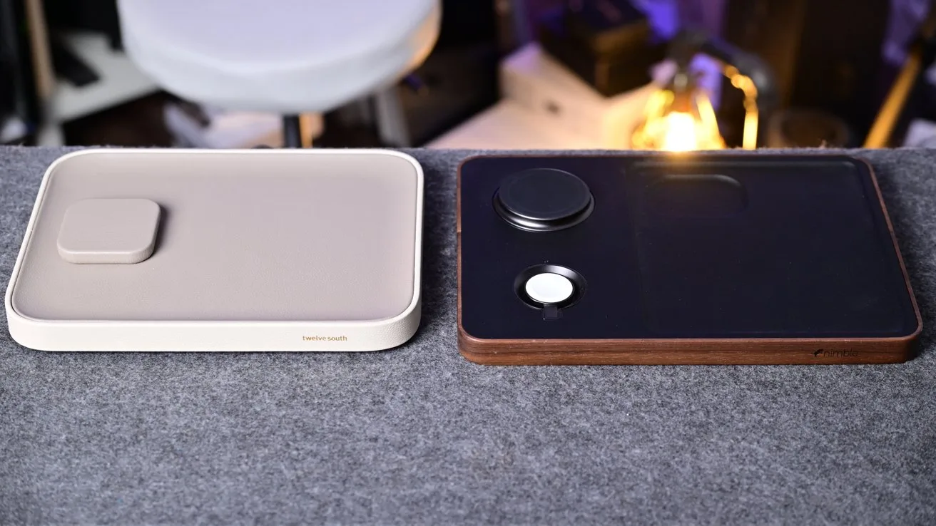 Two rectangular wireless charging pads on a gray surface, one beige and minimalist, the other black with wooden trim and circular charging spots, in a softly lit modern desk setup