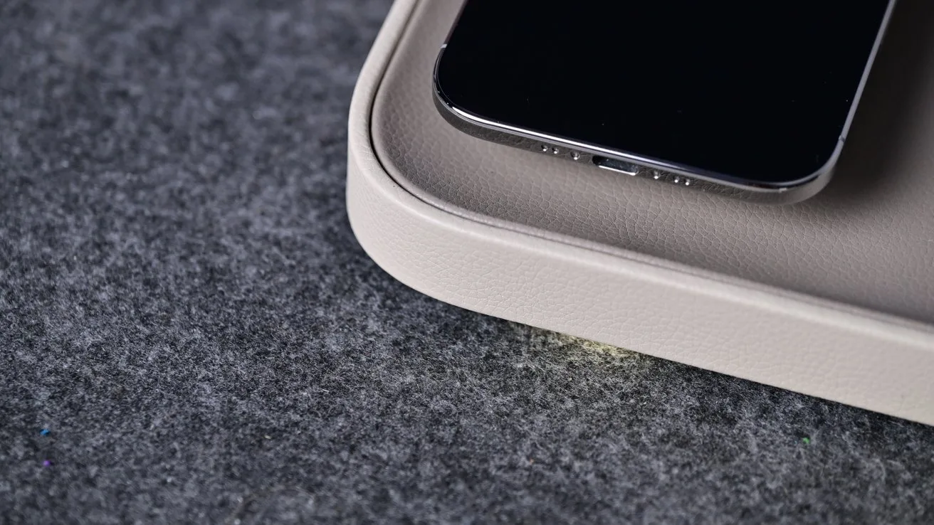 Smartphone resting on the corner of a light gray wireless charging pad, placed on a soft dark gray felt surface, viewed in close-up from above