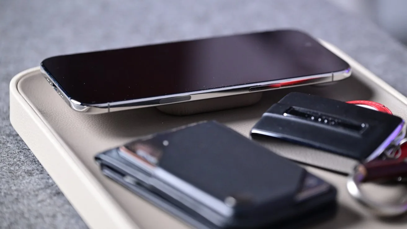Smartphone, wallet, car key fob, and keyring neatly arranged on a small tray resting on a gray fabric surface