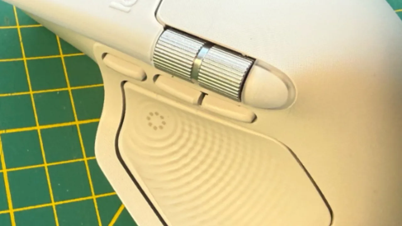 Close-up of a white ergonomic computer mouse with a textured thumb rest, two side buttons, and a silver scroll wheel on a green cutting mat.