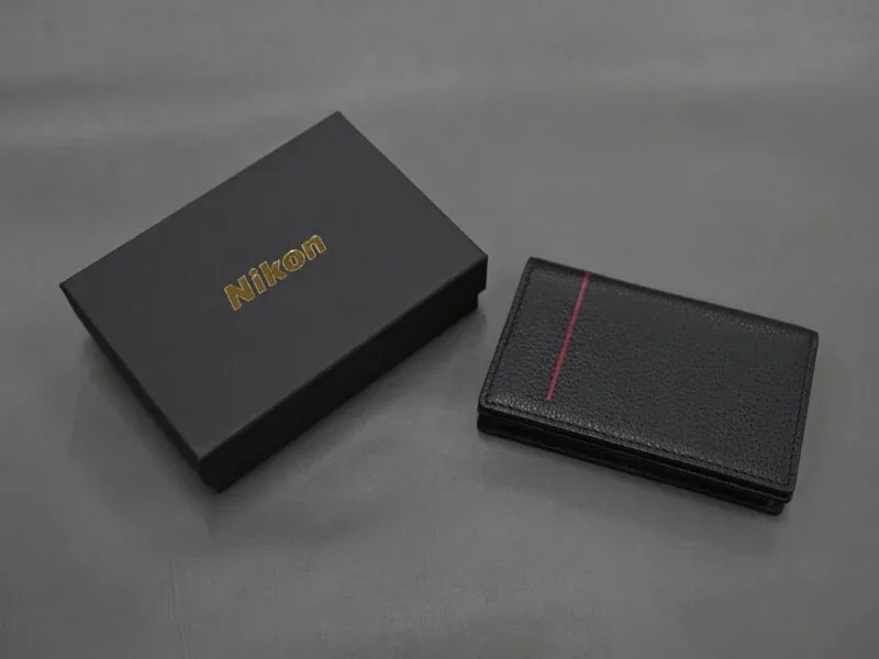 A black Nikon-branded gift box sits next to a black leather card holder with a single vertical red stripe.