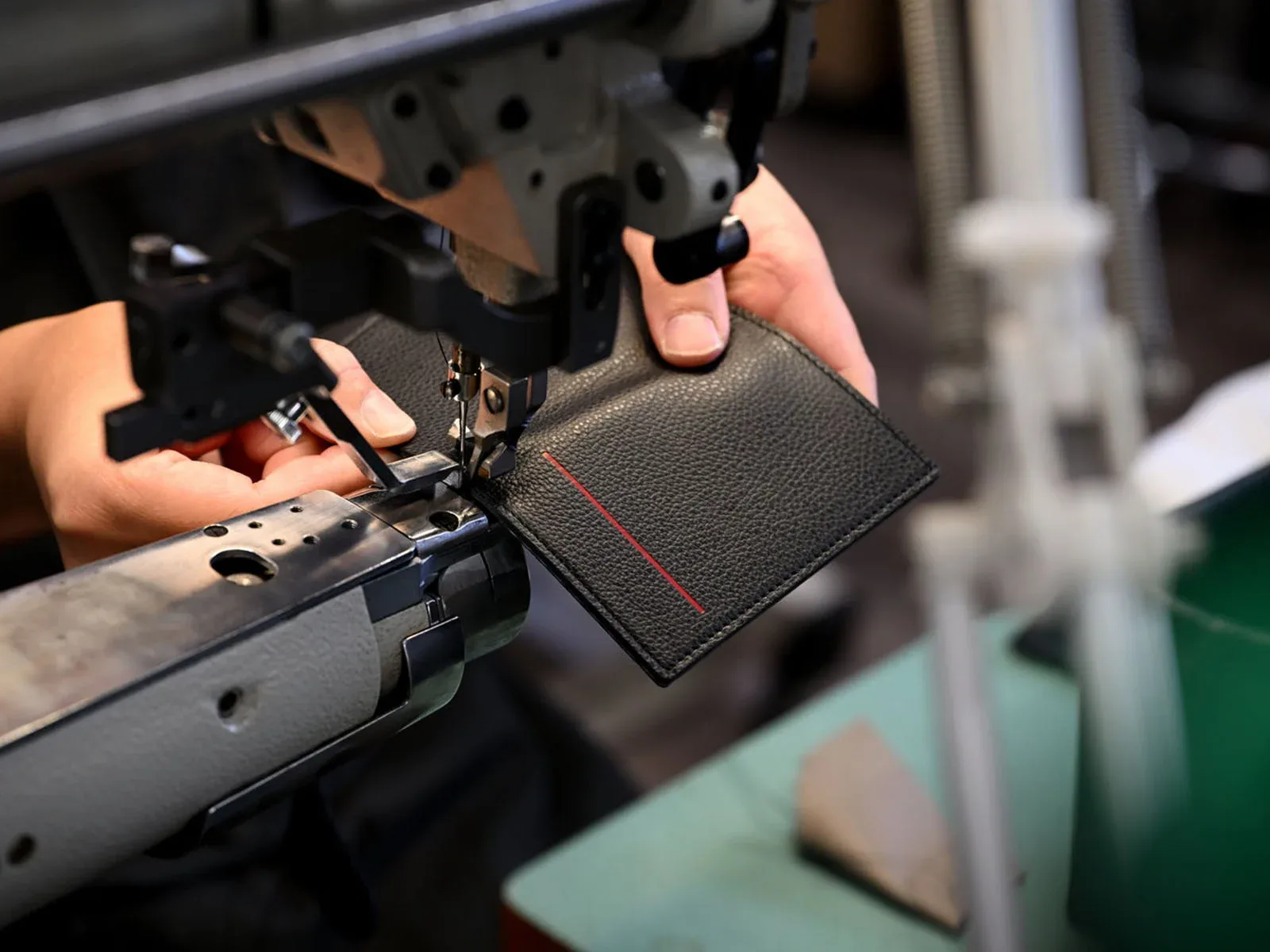 A person uses an industrial sewing machine to stitch a piece of black textured leather.