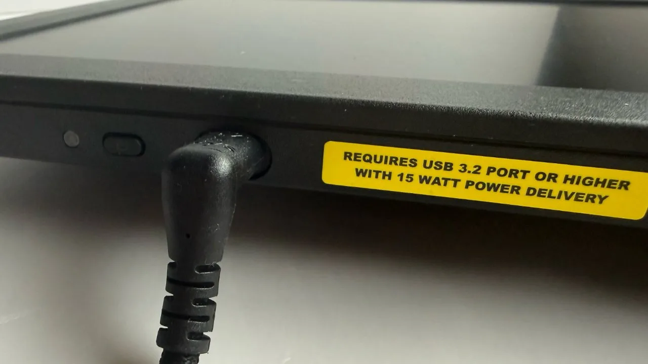 Close-up of a black electronic device with power cable plugged in and a yellow label stating requires USB 3.2 port or higher with 15 watt power delivery