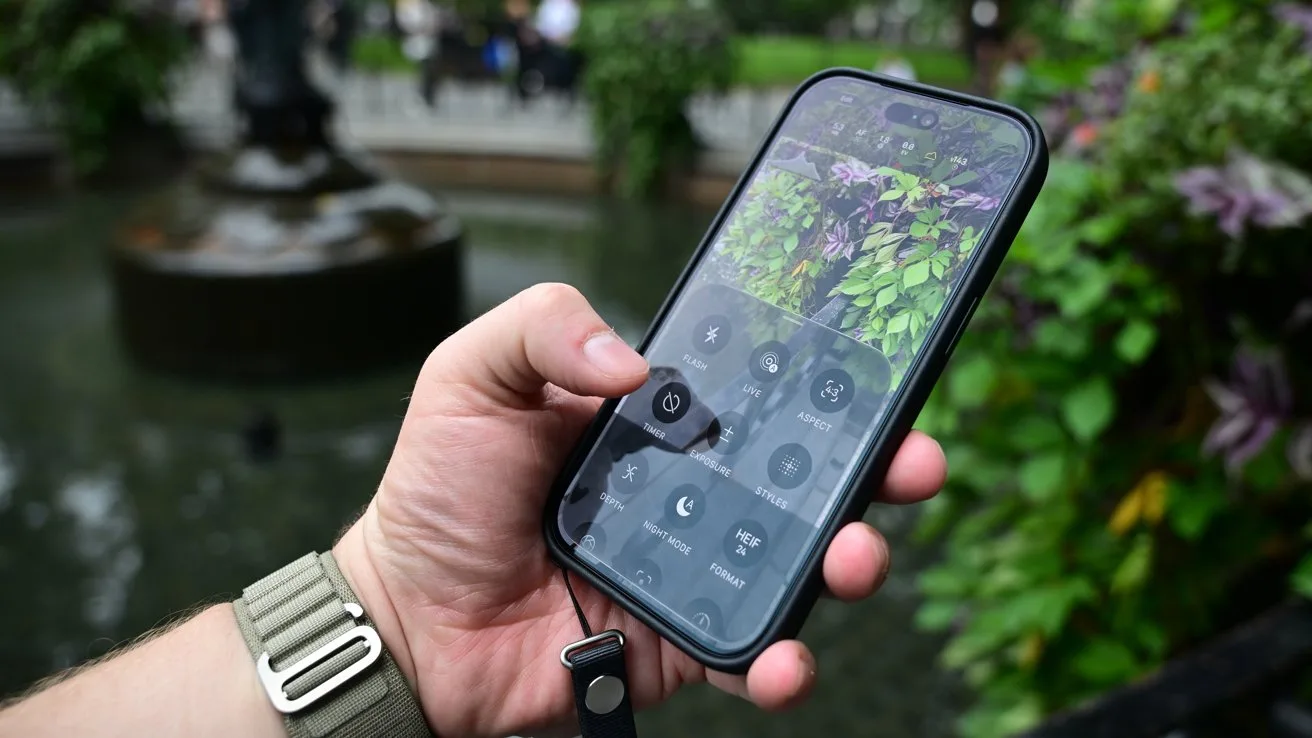 Hand holding a smartphone outdoors with control center icons on screen, reflecting green plants and flowers near a fountain, person wearing a green watch band and wrist strap attached to phone