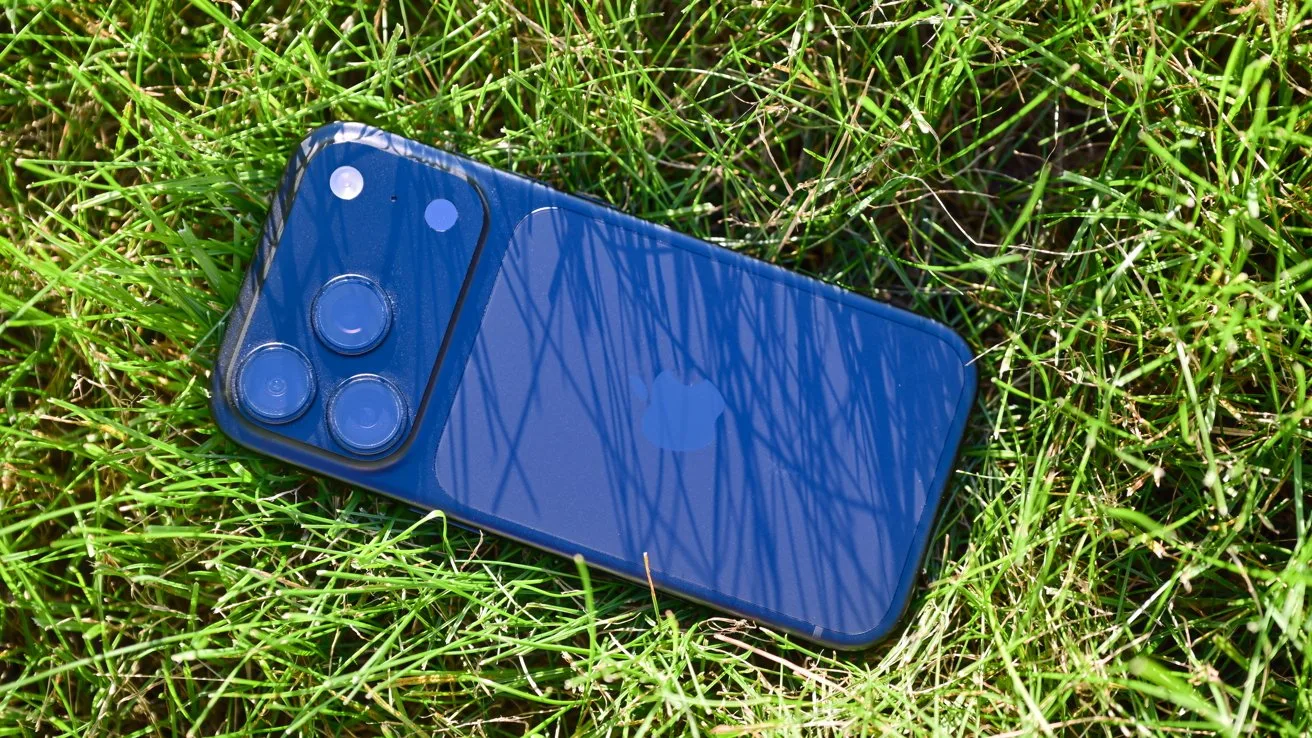 Blue smartphone lying face down on bright green grass, showing triple camera lenses and glossy back reflecting thin blades of grass