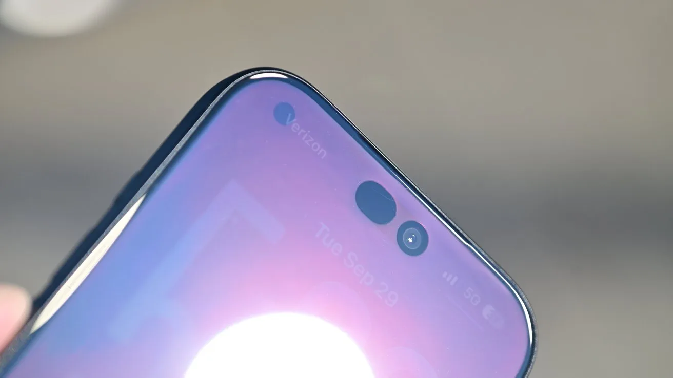 Close-up of a smartphone's top screen showing pill-shaped front camera cutout, glossy edges, and reflection of bright light on the display