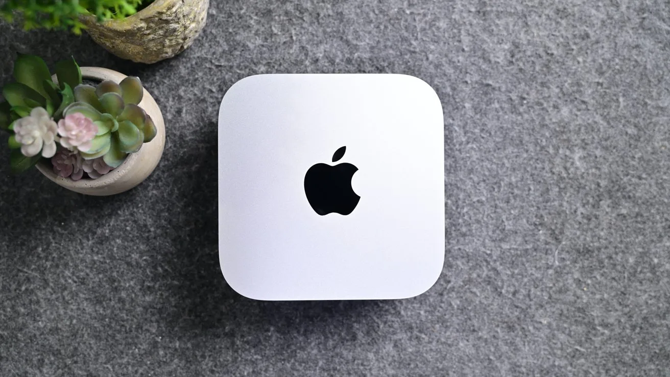 White Apple Mac mini on a gray felt surface, viewed from above, with small potted succulent plants placed nearby in the upper left corner