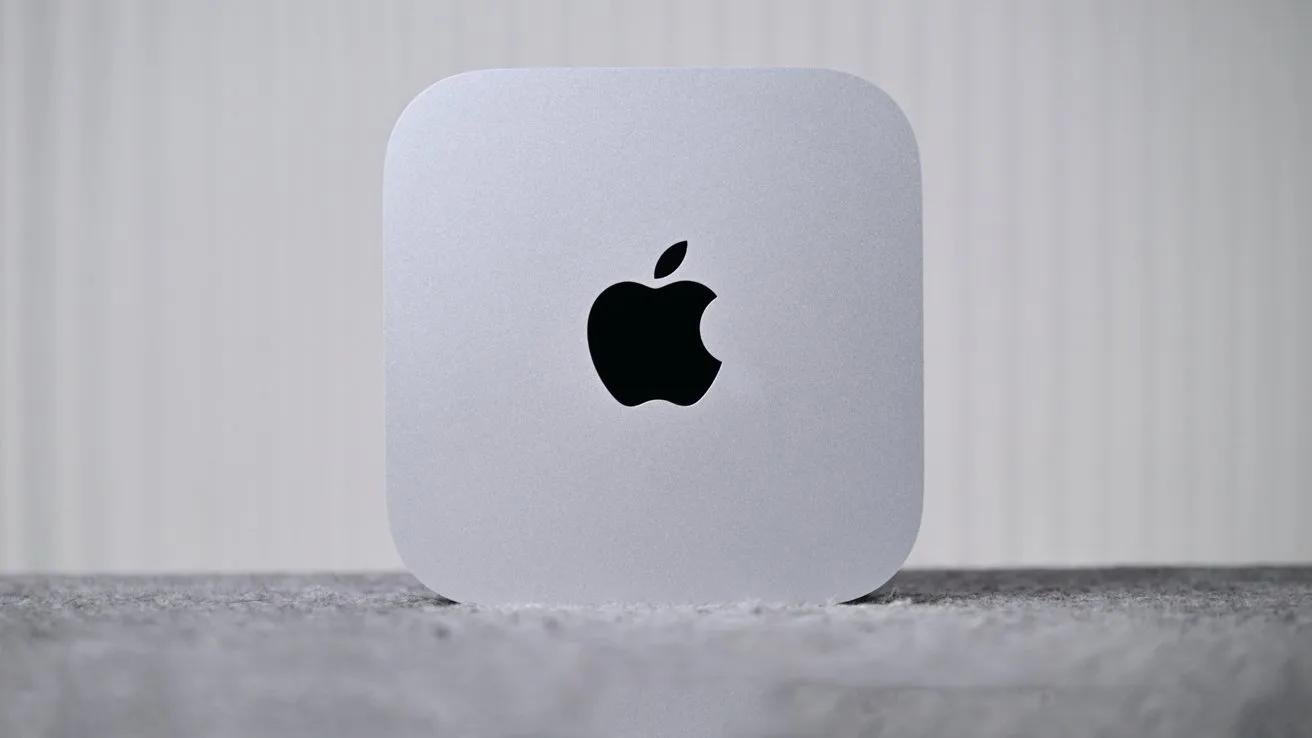 Silver Apple Mac mini computer with rounded corners, centered on a gray surface, showing a large black Apple logo against a softly lit, vertical-striped white background