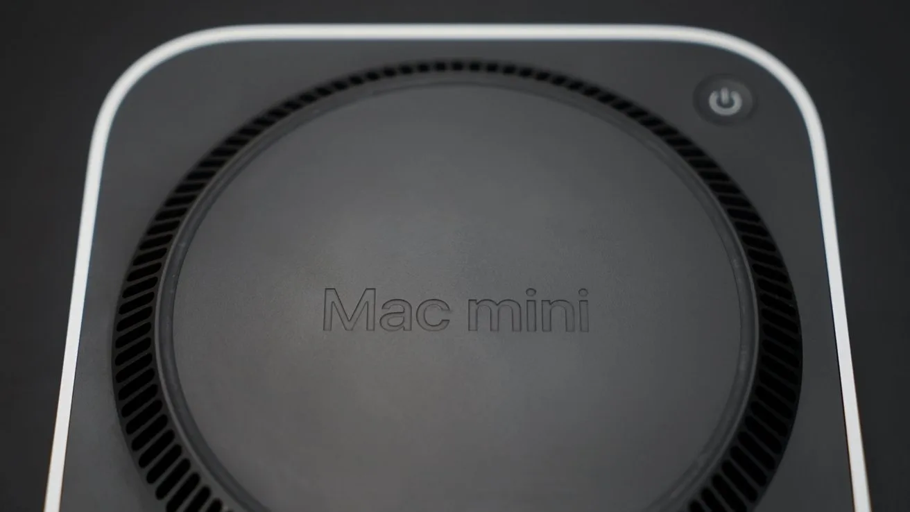 Top view of a Mac mini computer, showing the circular vented base with Mac mini text in the center and a small power button symbol near the edge
