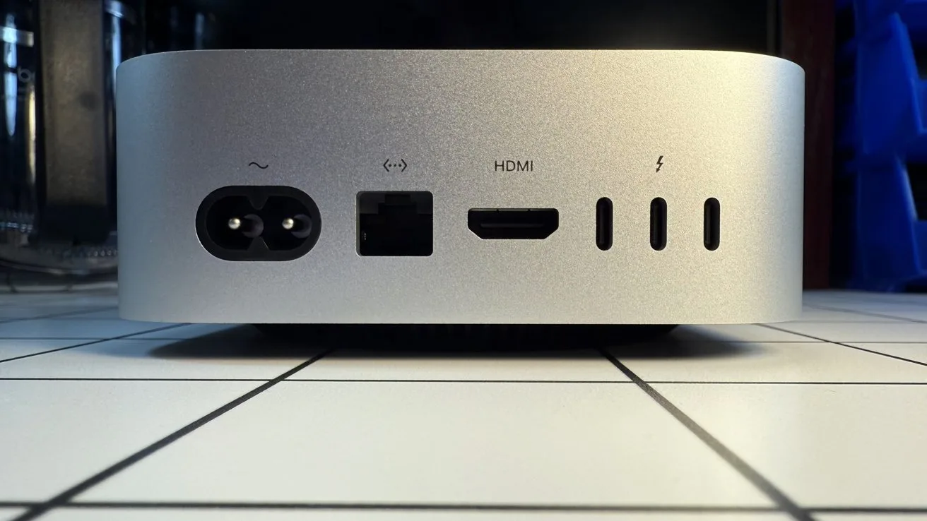 Small silver desktop computer on a tiled surface, rear view showing power connector, Ethernet port, HDMI port, and three Thunderbolt or USB-C style ports in a row