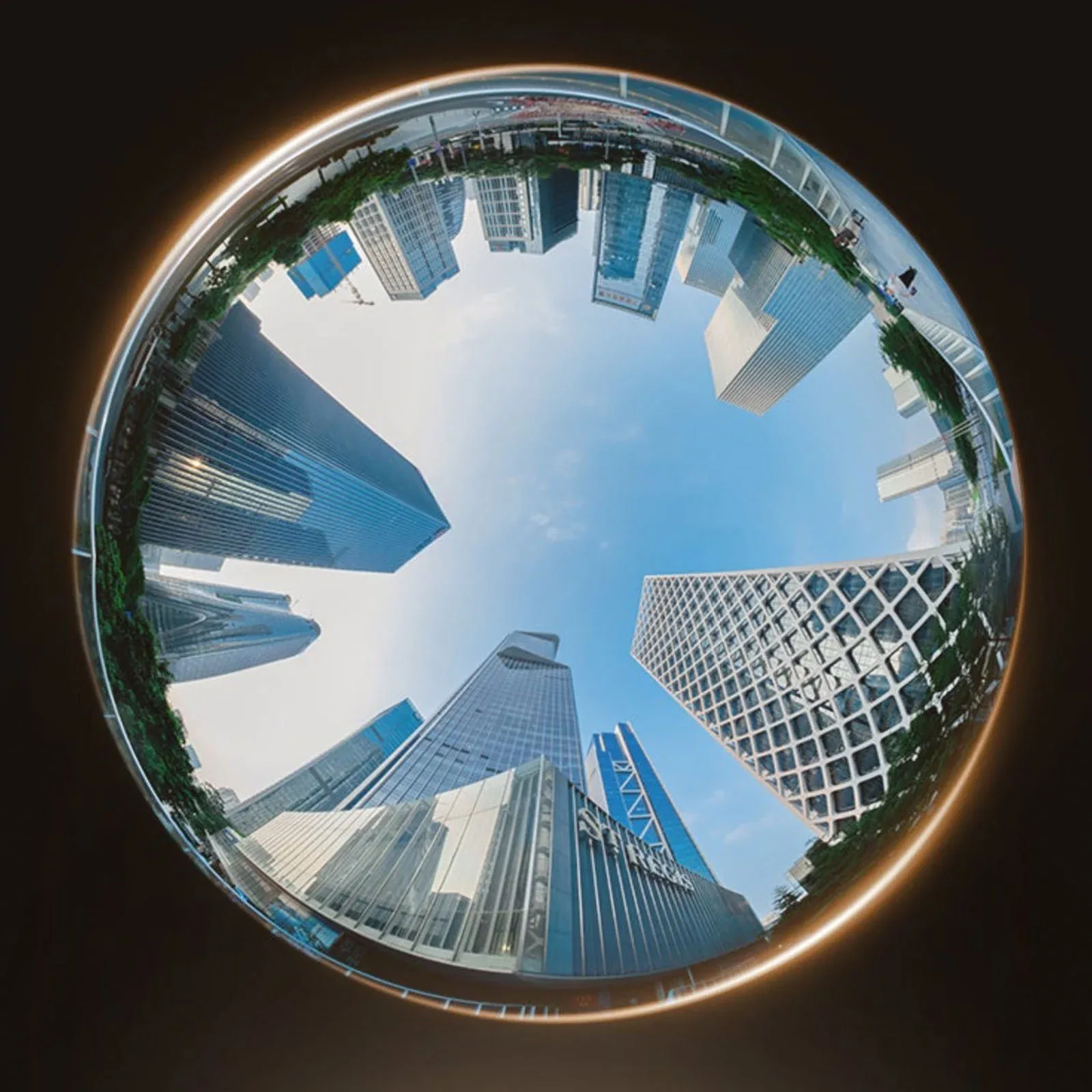 A fisheye view looking up at a circle of modern skyscrapers against a clear blue sky.